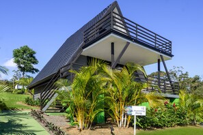A modern building with a sloped roof and a balcony, surrounded by lush greenery and a sign indicating a 'Humming Along' area. - Junglo Resort And Spa (Peñas Blancas)