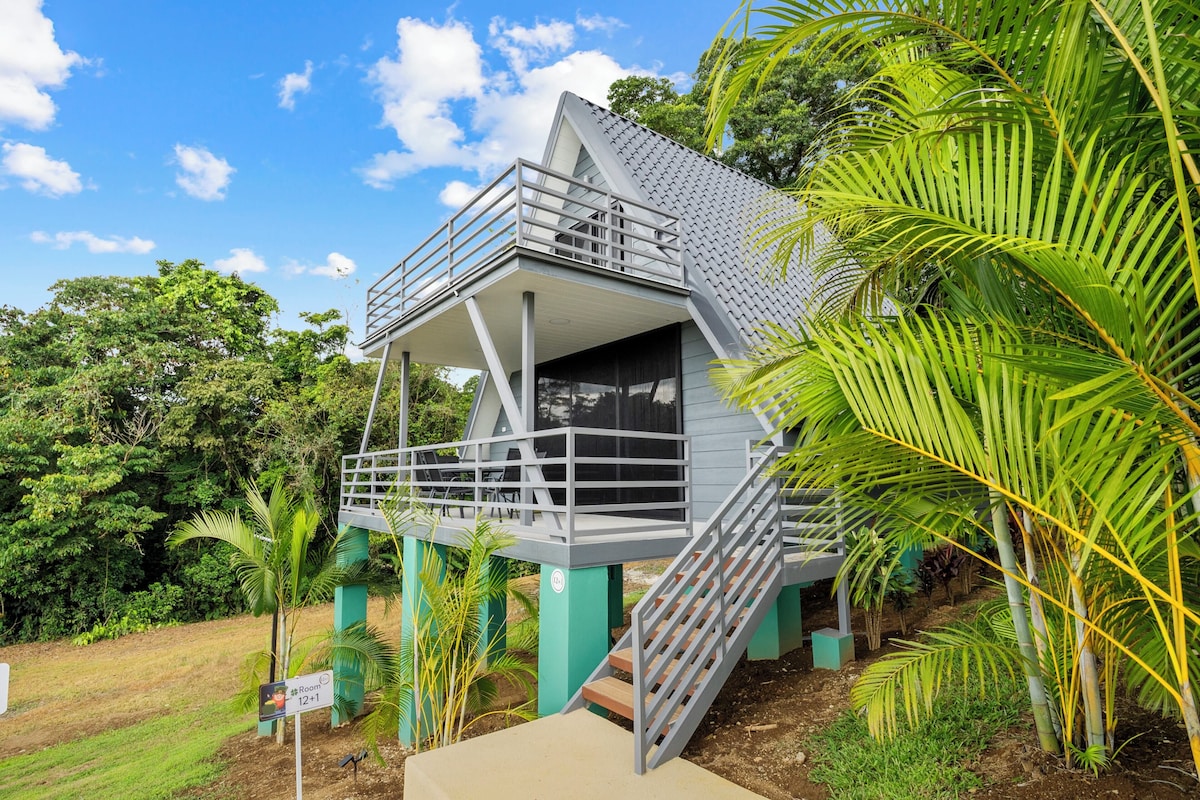 A modern building with a balcony and stairs, surrounded by lush greenery.