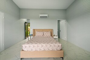 A bedroom with a bed, an air conditioning unit, a nightstand, and a door leading to another room.