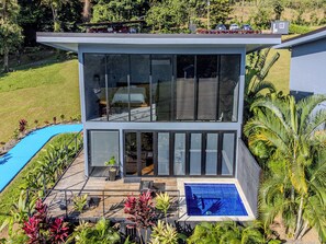A modern two-story house with a large glass window, a swimming pool, and tropical plants. - Junglo Resort And Spa (Peñas Blancas)