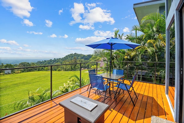 A balcony with a table and chairs, a blue umbrella, and a view of a green landscape. - Junglo Resort And Spa (Peñas Blancas)
