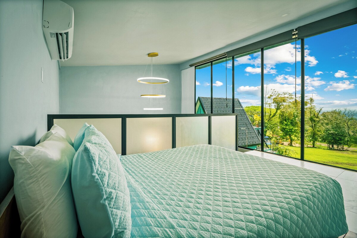 Un dormitorio con una cama grande, vistas al exterior y una lámpara de techo moderna.