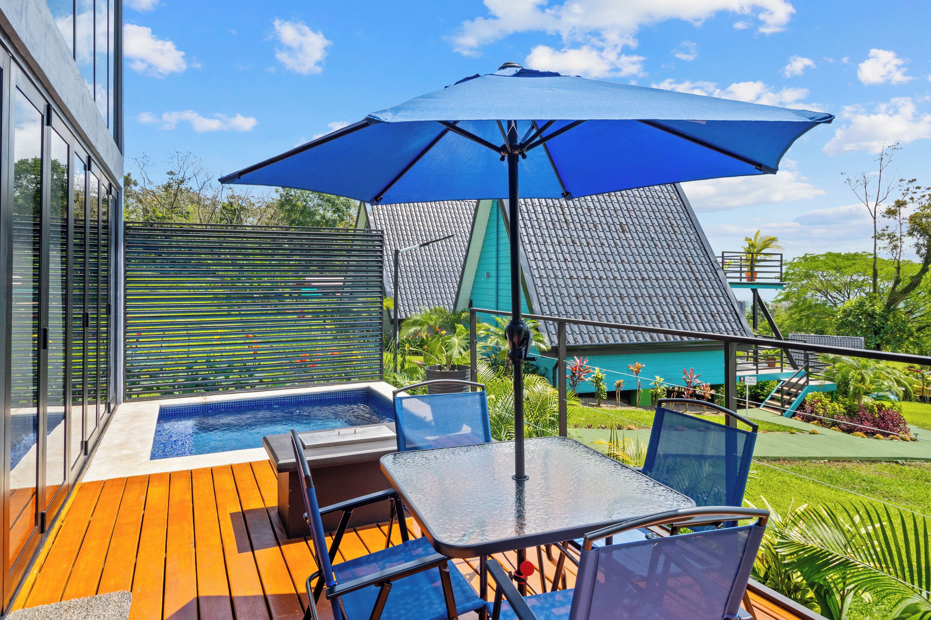 A poolside area with a hot tub, a table with chairs, and a blue umbrella.
