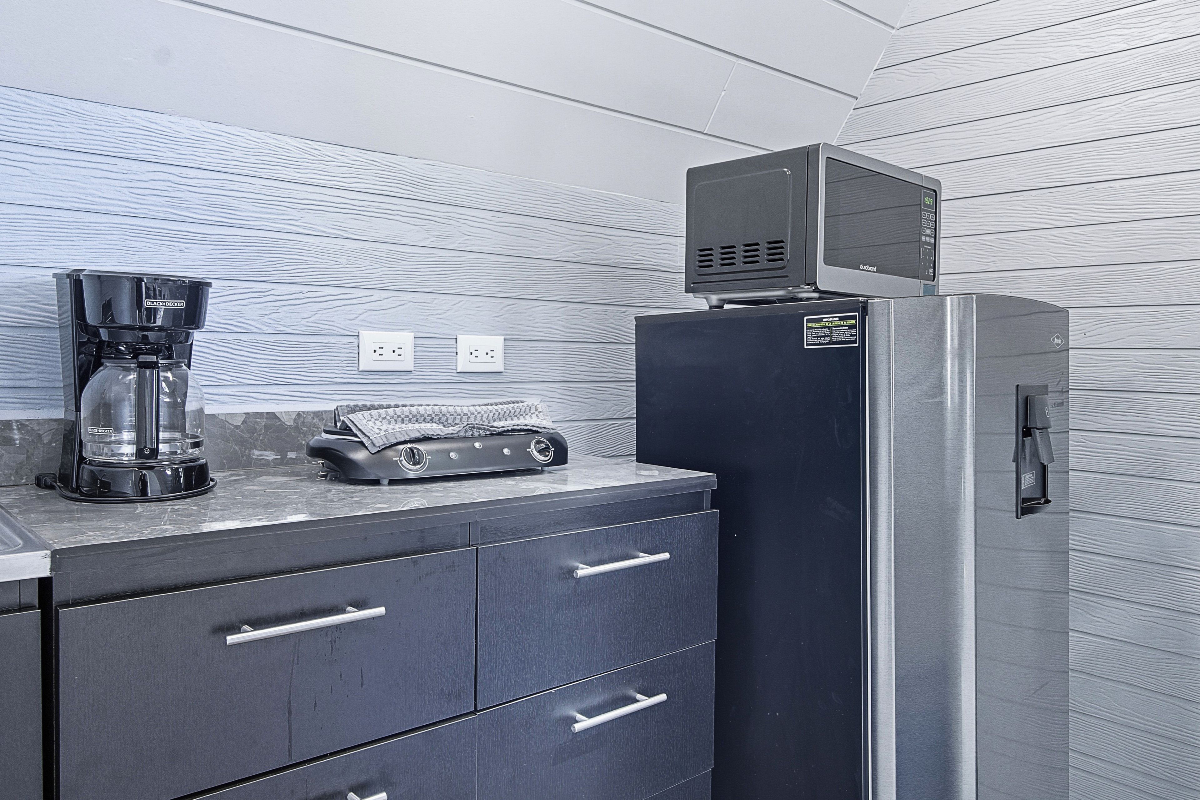 A kitchenette with a coffee maker, a microwave, and a refrigerator. There are two electrical outlets on the wall.
