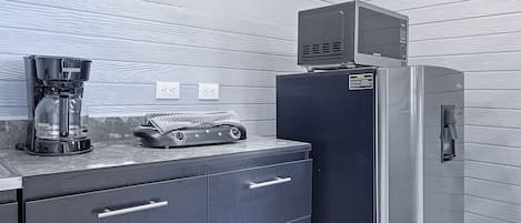 A kitchenette with a coffee maker, a microwave, and a refrigerator. There are two electrical outlets on the wall.