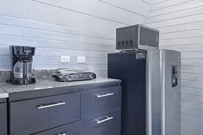 Una kitchenette equipada con cafetera, microondas y refrigerador. Hay dos tomas de corriente en la pared.