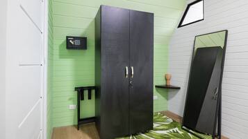 A room with a black wardrobe, a small black shelf, a mirror, and a green patterned rug.