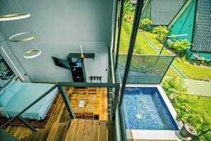 A room with a view of a swimming pool, a bed, a desk with a chair, and a hanging light fixture. - Junglo Resort And Spa (Peñas Blancas)