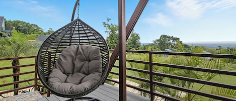 Een hangstoel op een houten terras met uitzicht op groen en een verre horizon.