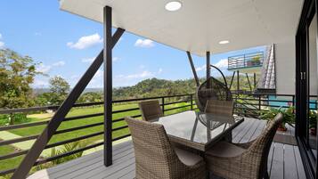 A balcony with a glass table and wicker chairs, overlooking a green landscape.