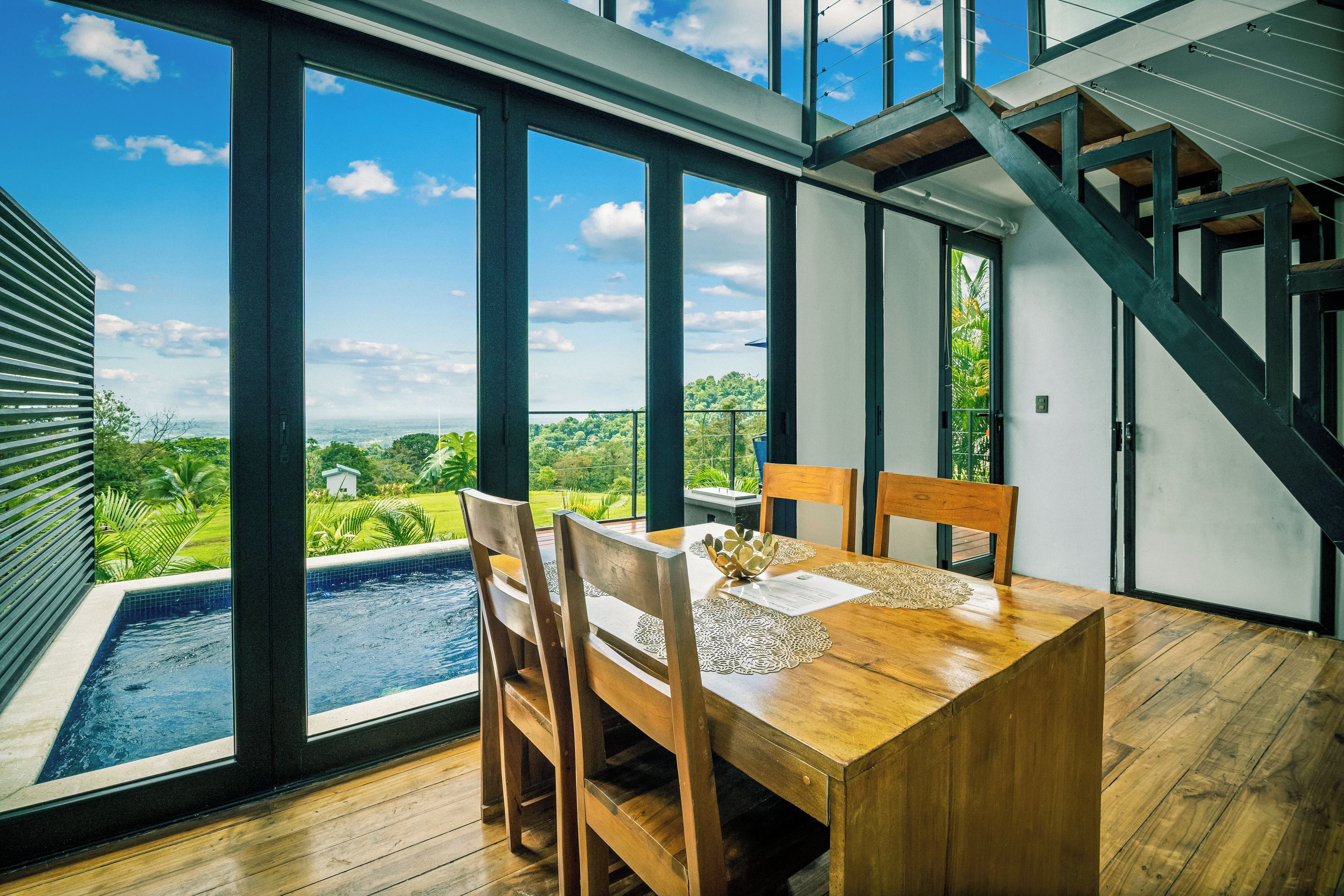 A dining area with a view of a swimming pool and greenery.
