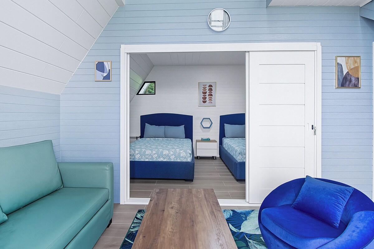 Un dormitorio con dos camas, un sofá verde, una silla azul y una mesa de madera.