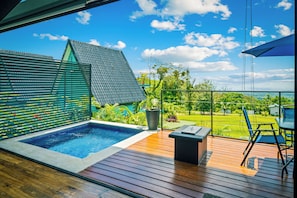 A modern outdoor pool area with a wooden deck, a hot tub, and a view of a lush garden and sky. - Junglo Resort And Spa (Peñas Blancas)