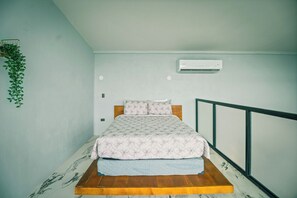 A single bed with a patterned bedspread and pillows, a wooden platform, a wall-mounted air conditioner, and a hanging plant. - Junglo Resort And Spa (Peñas Blancas)