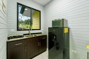A compact kitchen with a sink, dark wooden cabinets, a black refrigerator, and a window with a view of greenery. - Junglo Resort And Spa (Peñas Blancas)