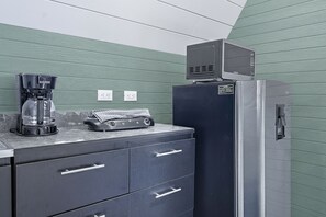 Una kitchenette con cafetera, microondas y refrigerador. Hay dos tomas de corriente en la pared.