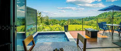 A poolside area with a view of a lush landscape, a table with a decorative bowl, and a patio with chairs and a table.