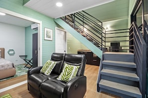 A living room with a black leather sofa, a staircase, and a kitchen area. - Junglo Resort And Spa (Peñas Blancas)