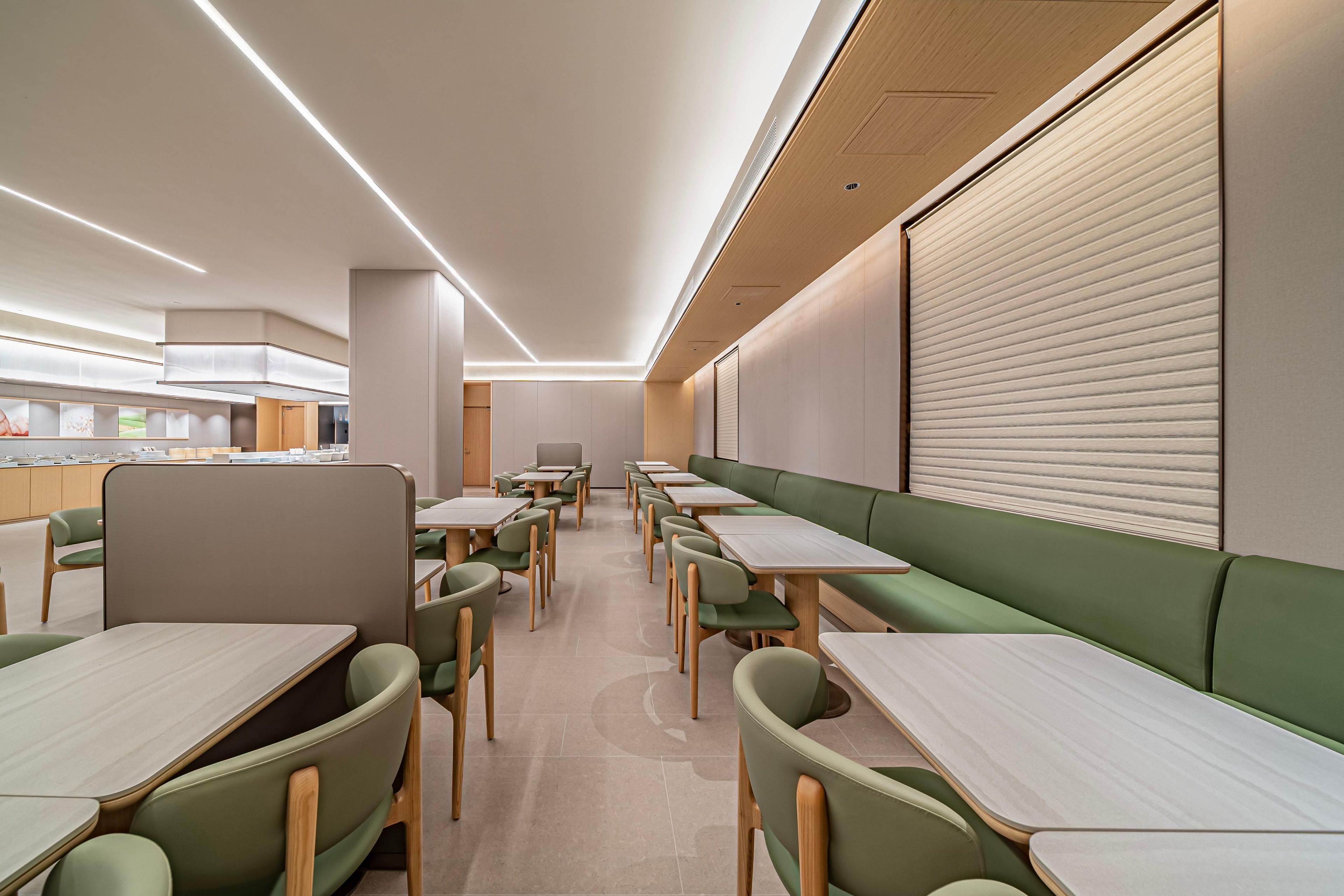Un'area ristorazione moderna con sedute a bancone e tavoli, caratterizzata da colori neutri e un design contemporaneo.