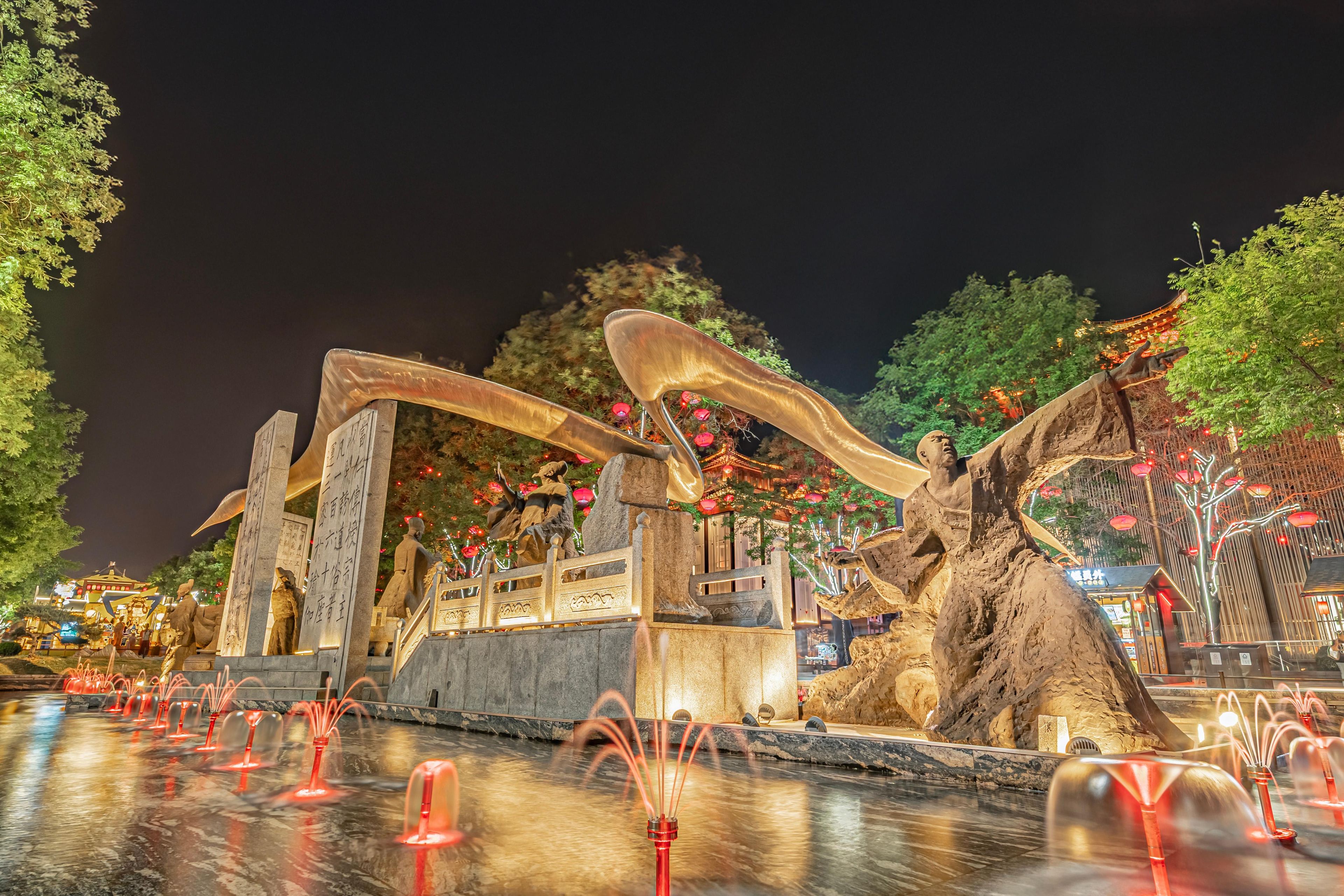 Een nachtelijke scène met een waterfontein, stenen beelden en traditionele architectuur.