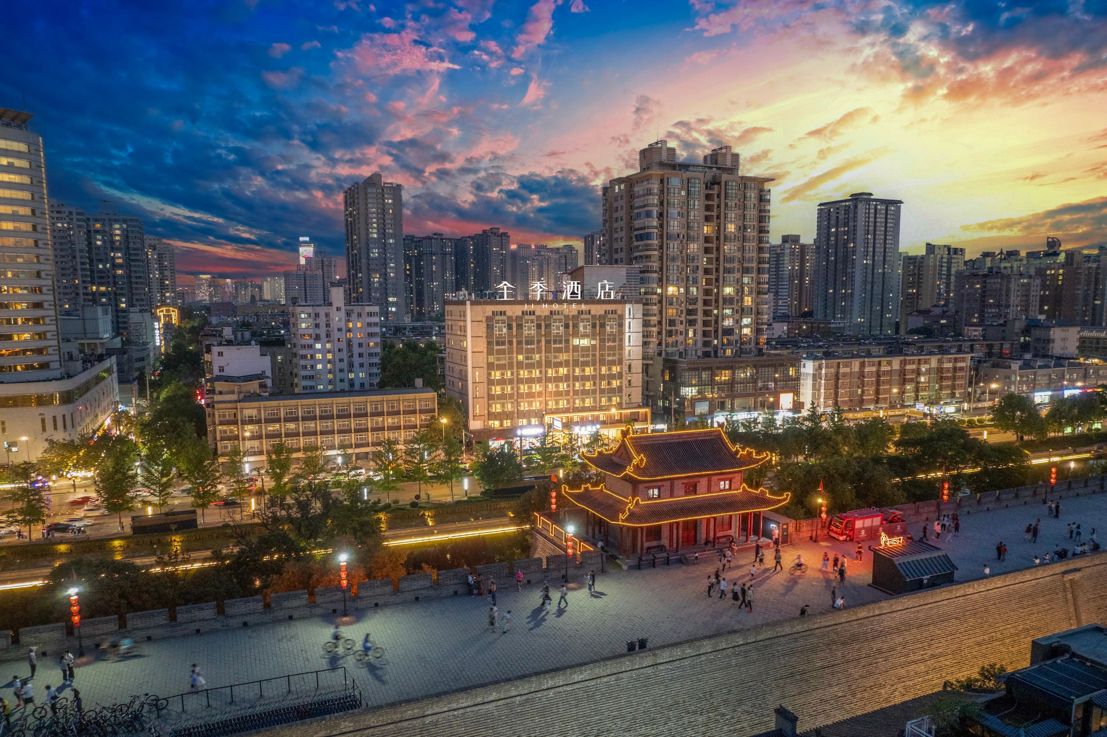 A hotel with a traditional architectural style, surrounded by modern high-rise buildings, and a pedestrian area with people and bicycles.