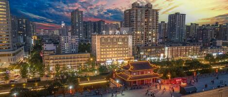 A hotel with a traditional architectural style, surrounded by modern high-rise buildings, and a pedestrian area with people and bicycles.
