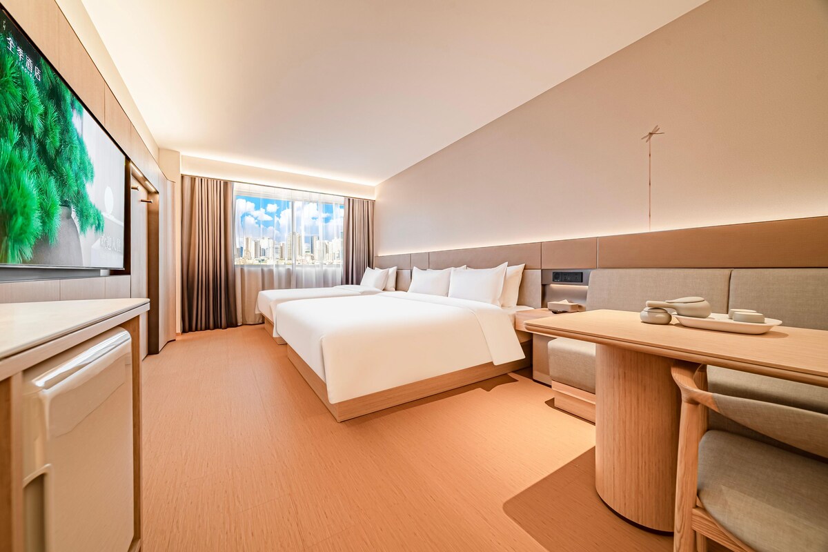 A hotel room with a bed, a desk, a television, and a view of the city.