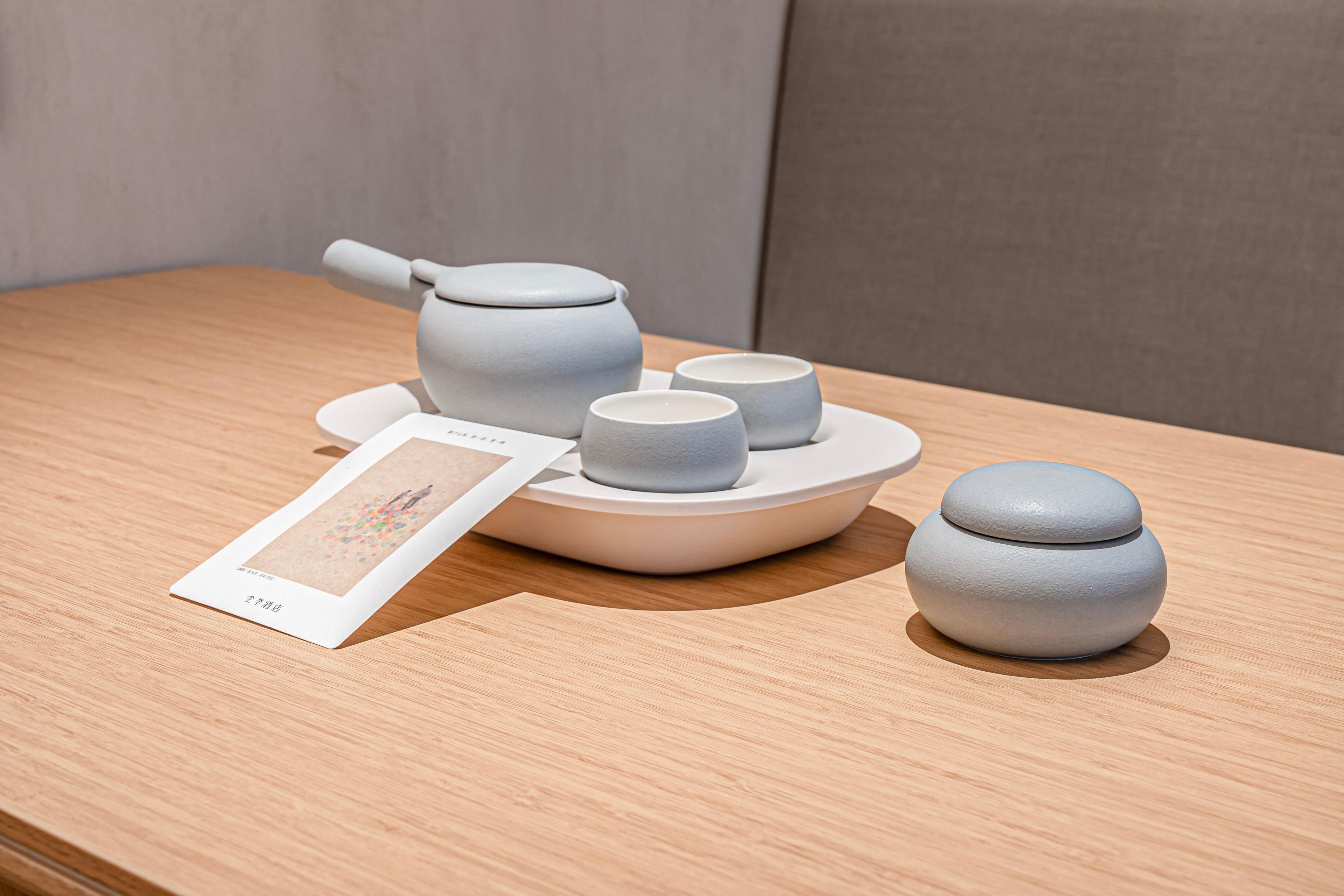 Un service à thé comprenant une théière, des tasses et un petit récipient, le tout posé sur une table en bois.