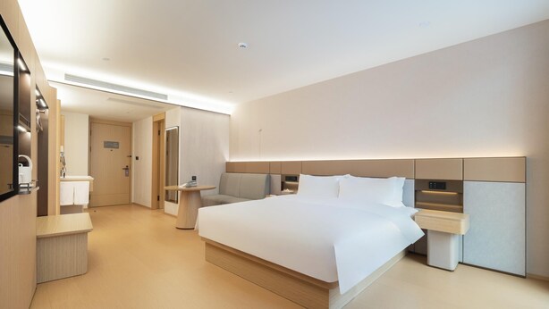 Une chambre d’hôtel moderne dotée d’un grand lit, de tables de chevet, d’un bureau intégré et d’une salle de bain séparée.