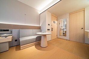Habitación de hotel moderna con sofá, una mesa redonda, un espejo y un armario.