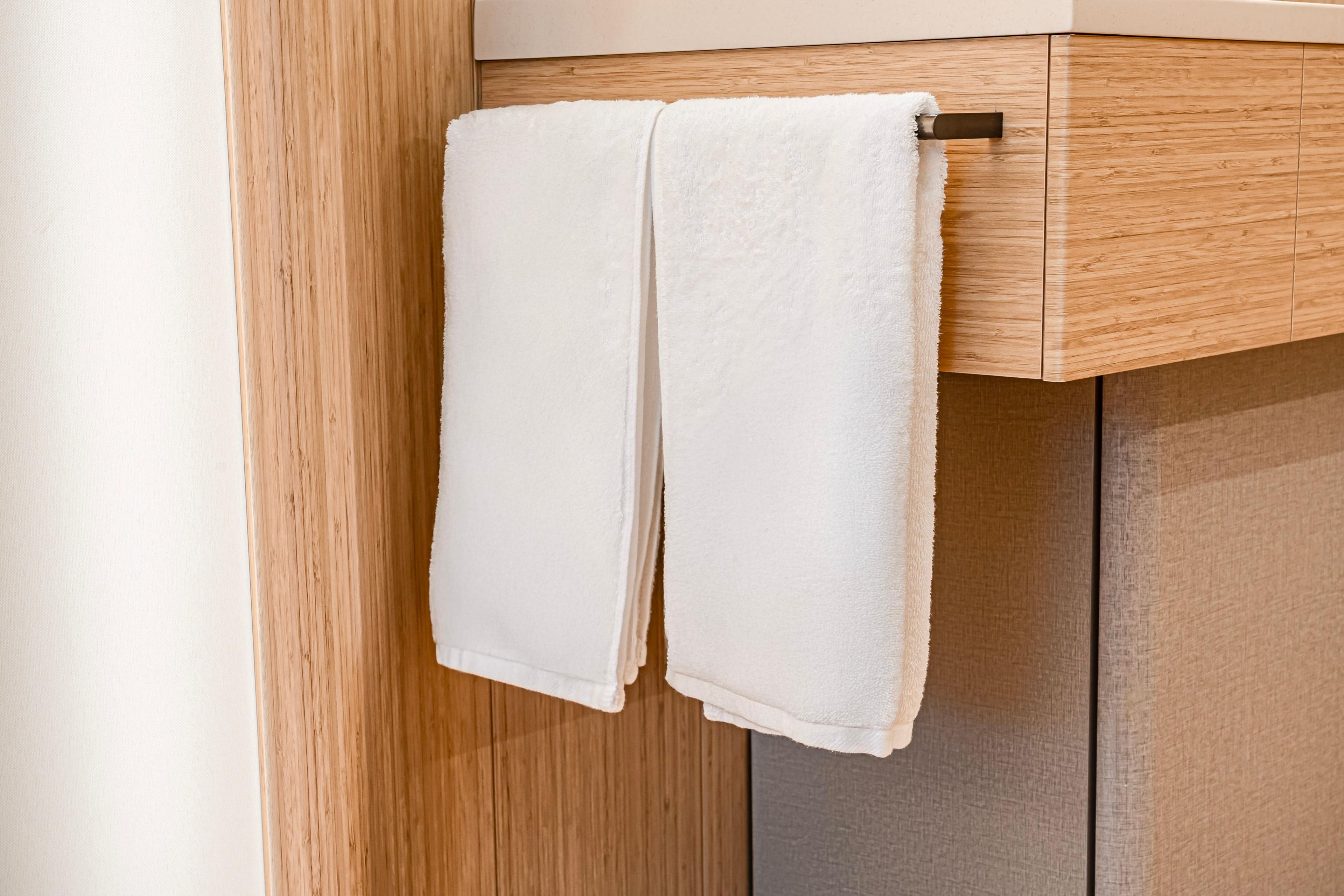 A white towel hanging on a wooden towel rack in a bathroom.