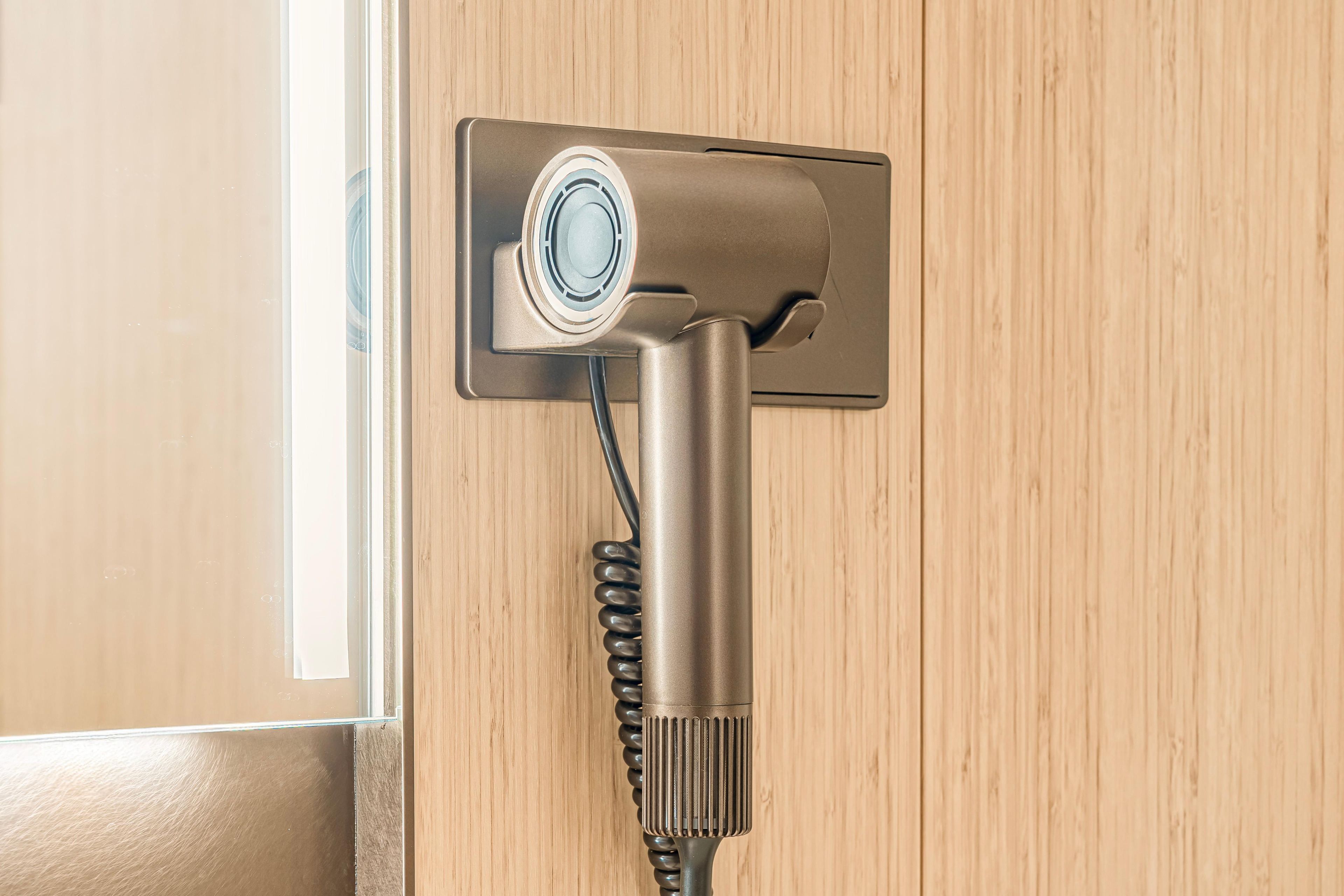 A hair dryer mounted on a wall with a cord.