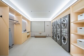 Een moderne wasserij met een rij gestapelde wasmachines, een bankje en een wandgedragen droogrek.