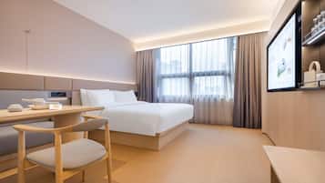 A modern hotel room with a bed, a desk, a chair, and a TV screen displaying a menu.