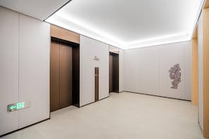 A modern elevator area with two elevators, a wall-mounted sign, and a floor with a light-colored finish. - JI Hotel (Xi'an)