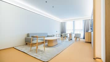 A modern hotel room with a sofa, chairs, a coffee table, and a small side table.