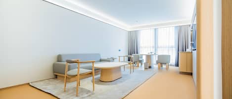 A modern hotel room with a sofa, chairs, a coffee table, and a small side table.