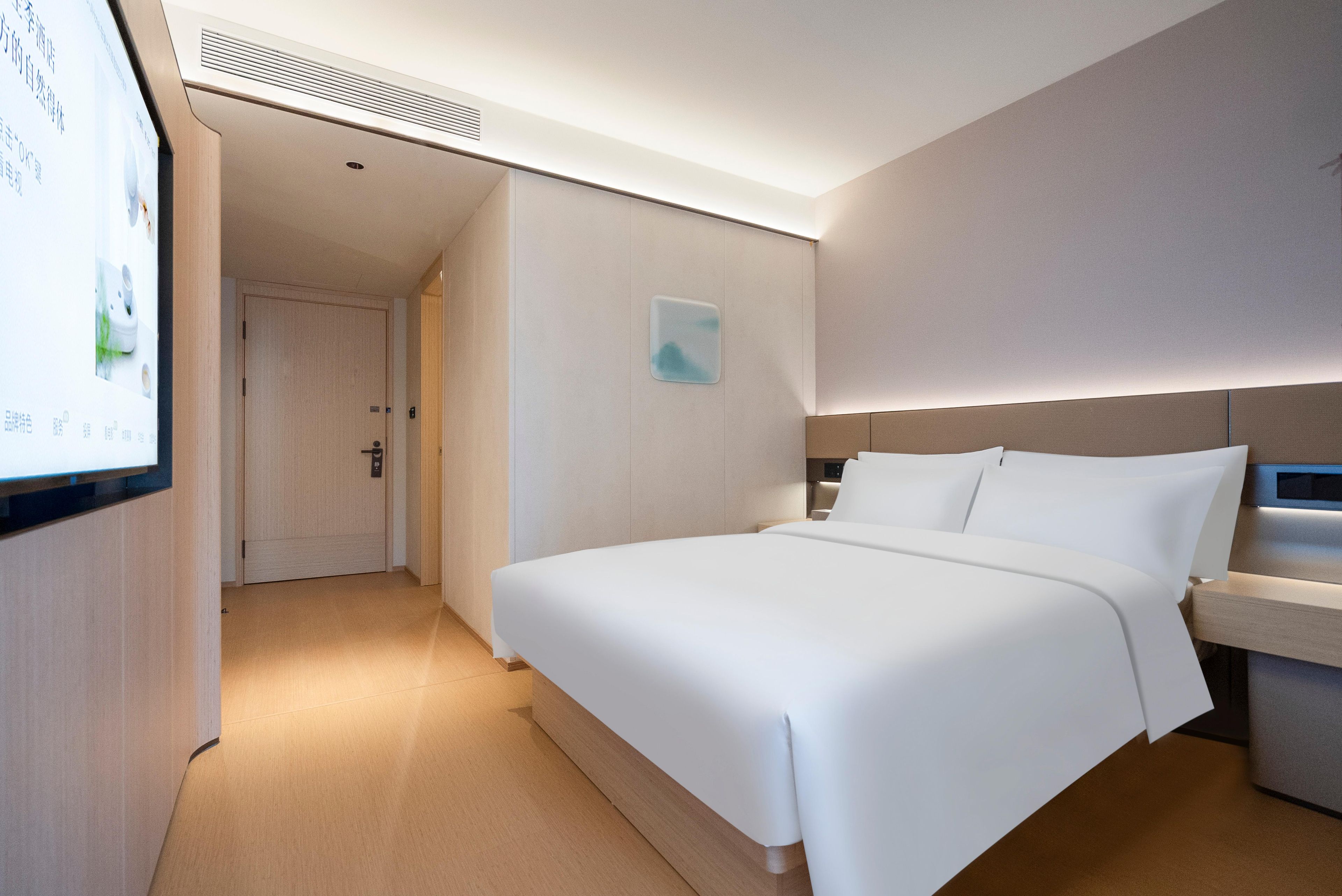 A hotel room with a large bed, a bedside table, a wall-mounted TV, and a door leading to another room.