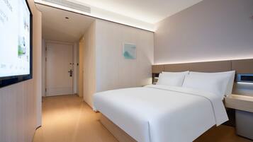 A hotel room with a large bed, a bedside table, a wall-mounted TV, and a door leading to another room.