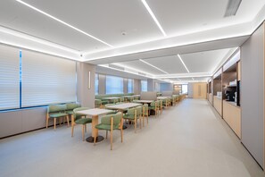 Un interior moderno con mesas y sillas largas, un largo pasillo y una zona de kitchenette.