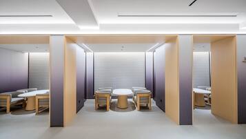 A modern, well-lit room with a central round table, four chairs, and a partitioned area with a bench.