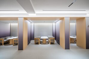 Quarto moderno e bem iluminado, com uma mesa redonda central, quatro cadeiras e uma área dividida com um banco.