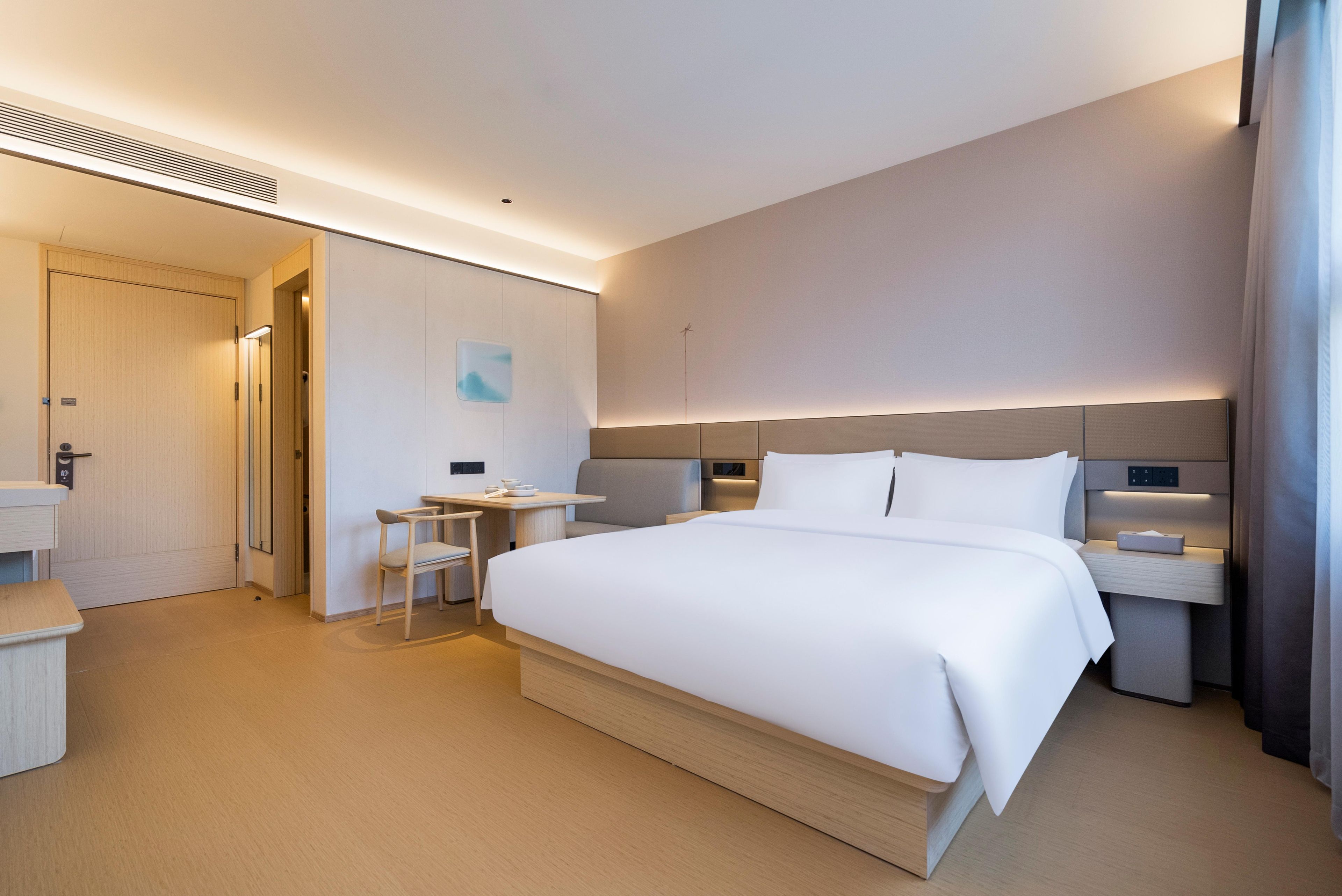 A modern hotel room with a large bed, bedside tables, a small desk, and a chair.