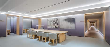 Une salle de conférence moderne, dotée d’une longue table et de chaises, d’un grand tableau abstrait et d’un couloir menant à une autre pièce.
