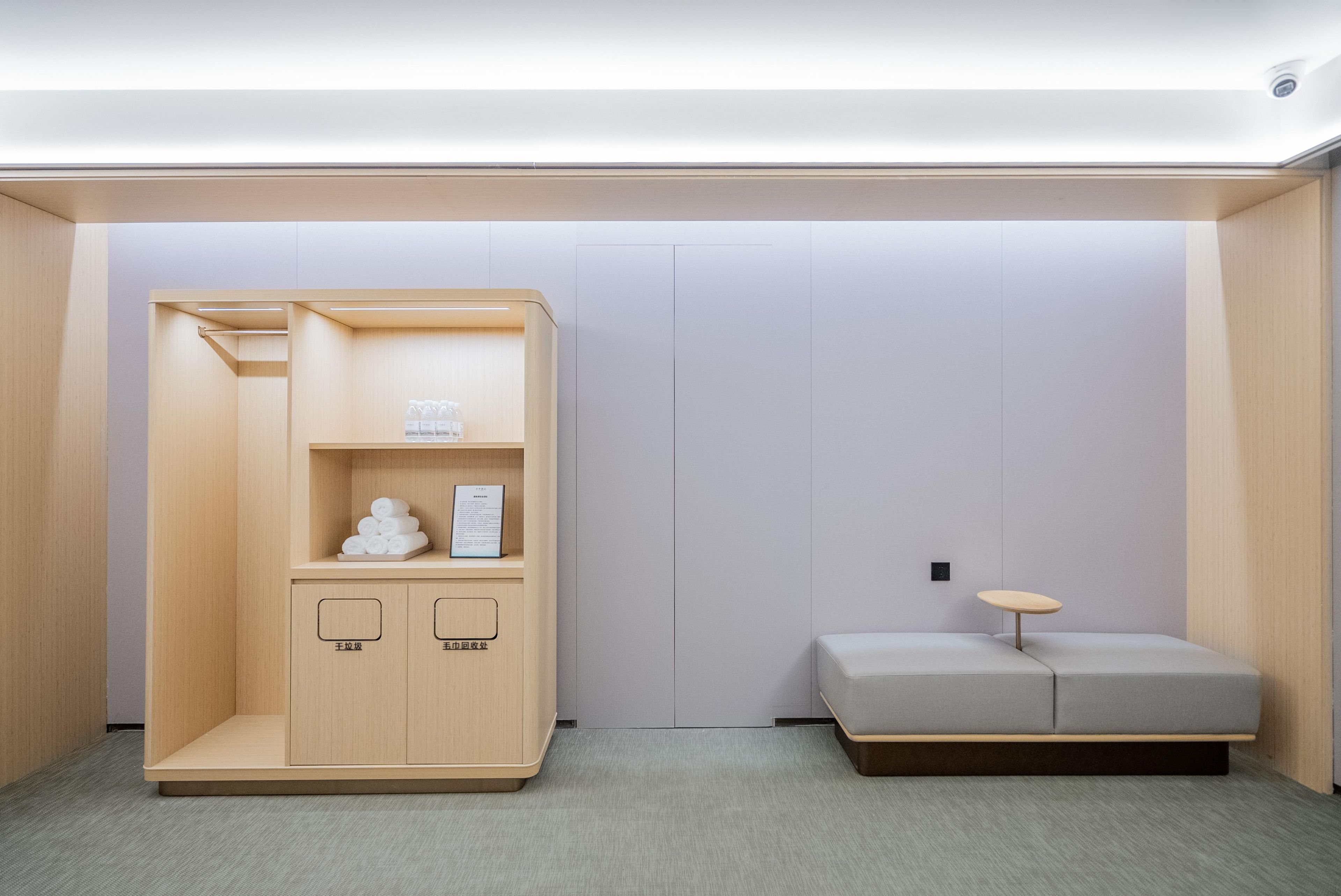 Een kleine kamer met een houten garderobe, een tafeltje en een grijze bank.