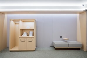 Een kleine kamer met een houten garderobe, een tafeltje en een grijze bank.