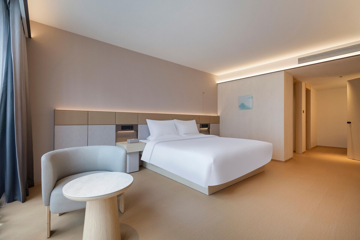 A modern hotel room with a bed, a small round table, a chair, and a nightstand.