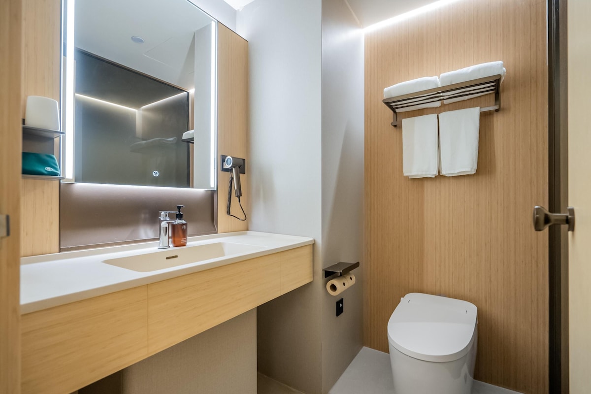 A modern bathroom with a large mirror, a sink, a toilet, and a towel rack.
