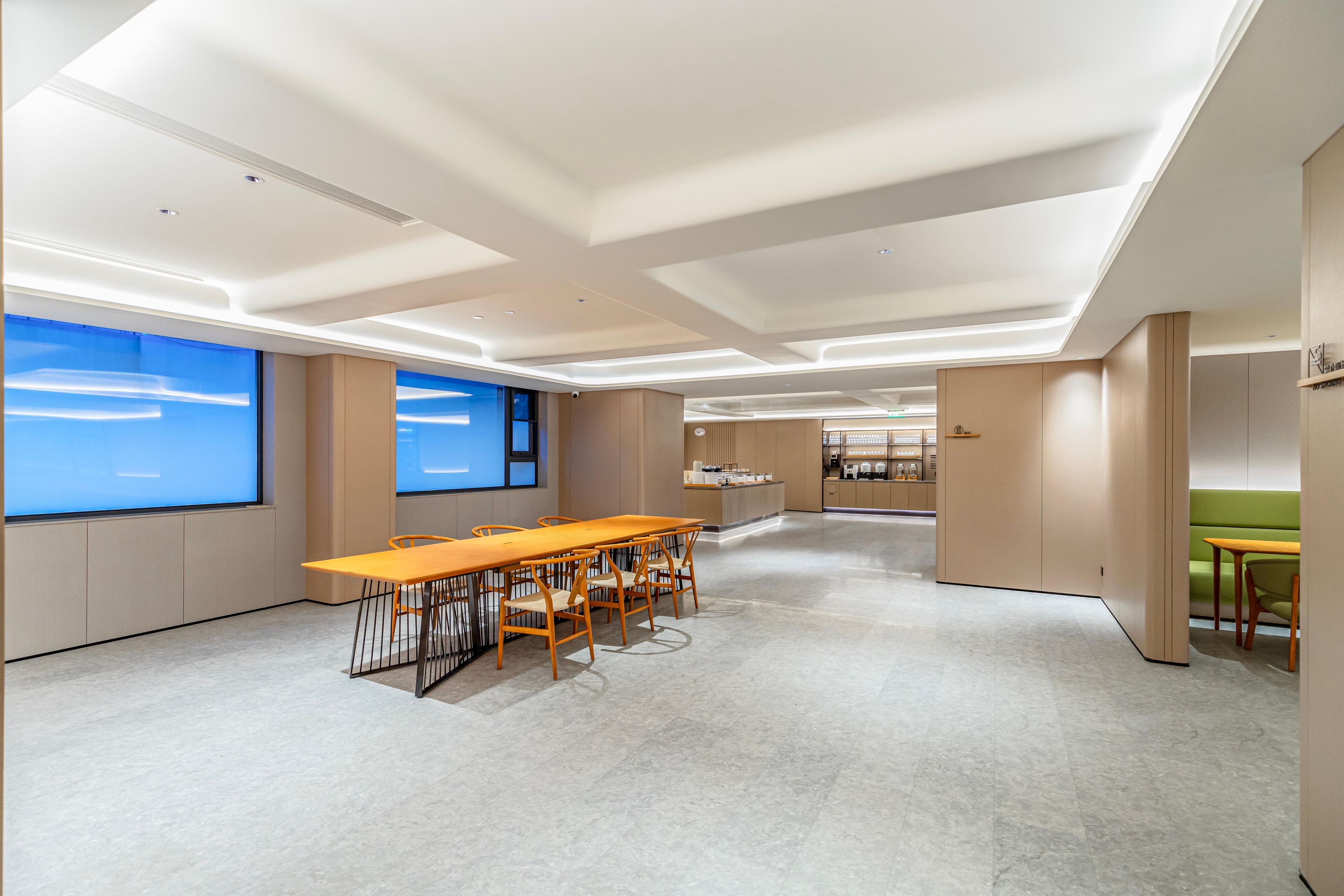 A modern conference room with a long table, chairs, and a view of the sky through large windows.