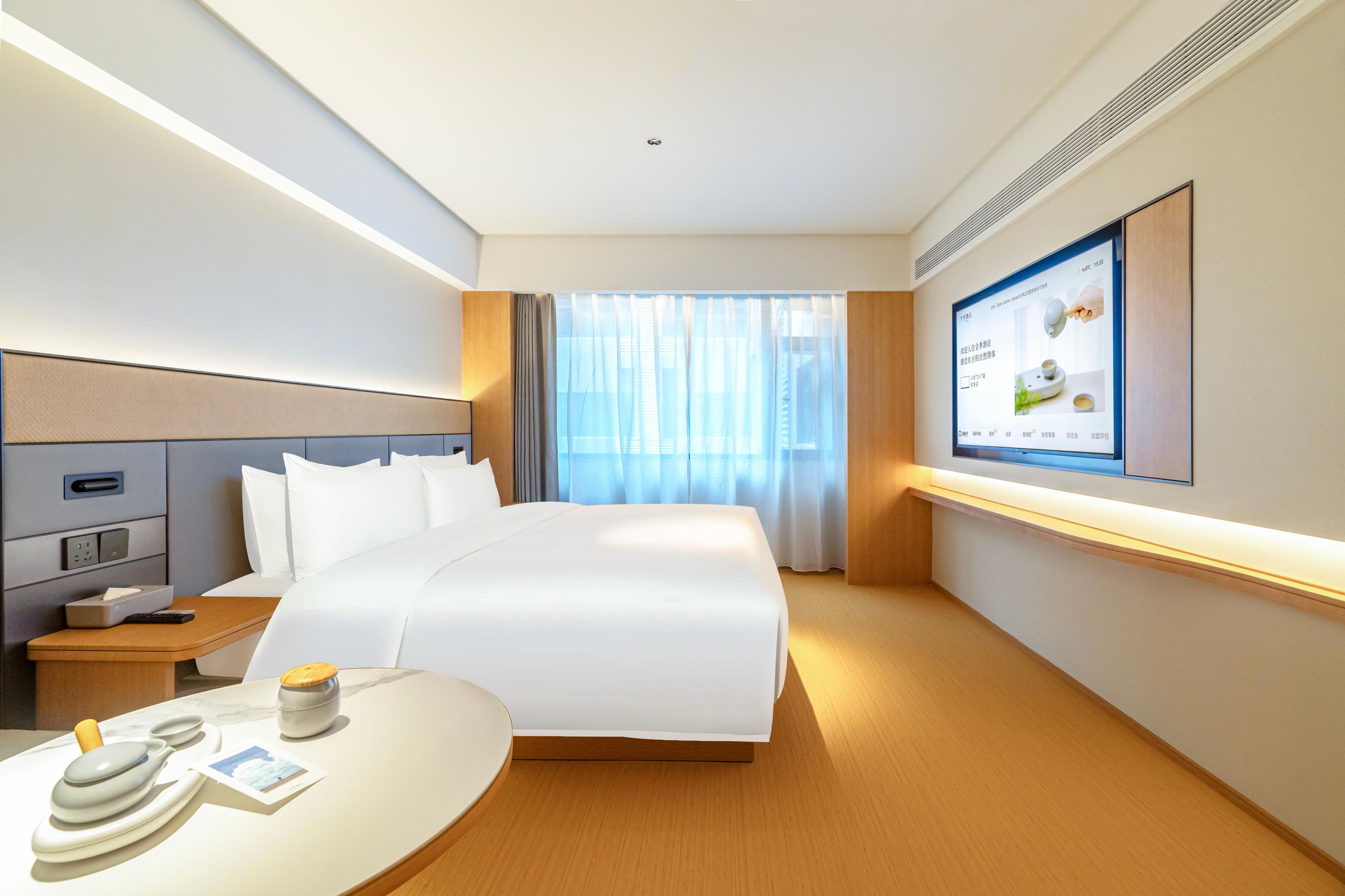 Quarto de hotel com cama, mesa de cabeceira, televisão e janela com cortinas.